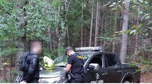 Policjant wykonuje czynności z mężczyzną, który jeździł w lesie na motocyklu crossowym.