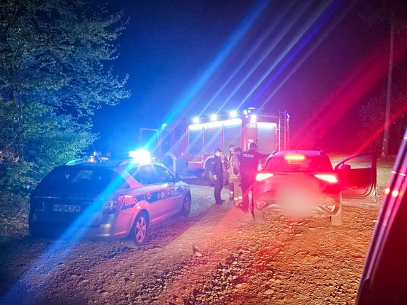 Radiowóz z włączoną sygnalizacją świetlną nocną porą, obok straż pożarna i samochód osobowy