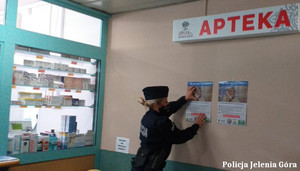 Policjantka wiesza plakat dot. oszustw na szkodę seniorów