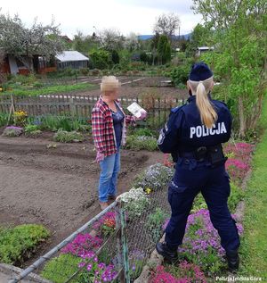 Policjantka rozdaje działkowcom ulotki prewencyjne